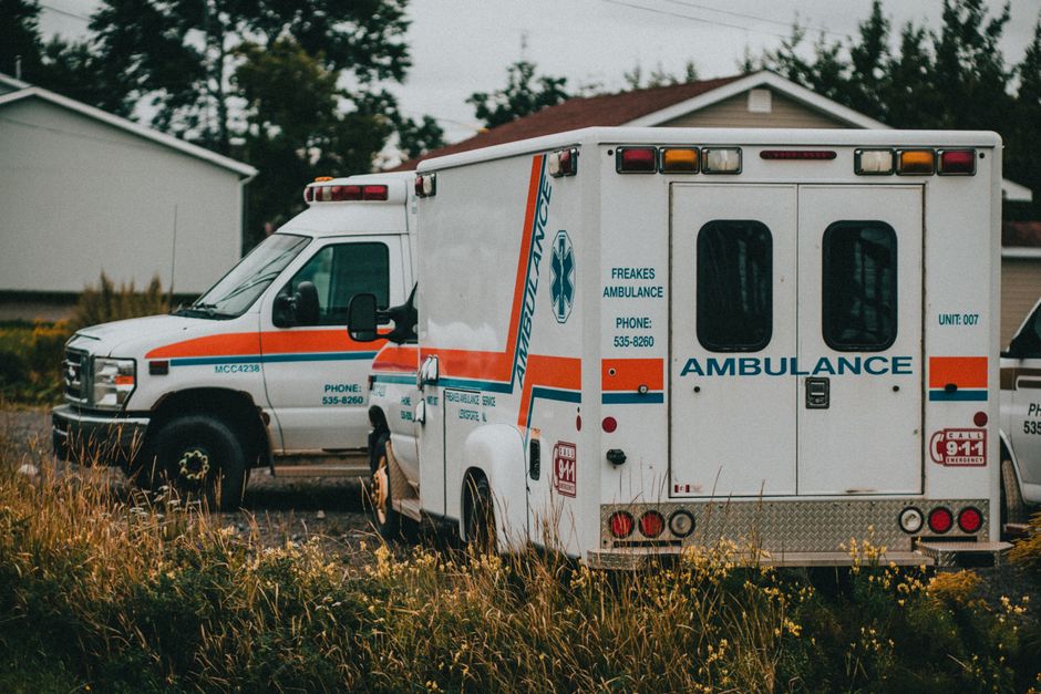 A white ambulance vehicle with red stripes and the Chicago Fire Department emblem on the side, equipped with emergency lights that are flashing red and white, is moving rapidly along a wet road at nig